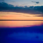Tranquil-sunset-reflects-soft-colors-over-calm-water-horizon