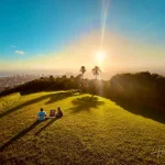 Picturesque Sunset Romance on a Hill Couple-sitting-on-green-hill-overlooking-city-sunset