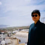 Lu Heng Standing Outdoors with Scenic White Coastal Village View Luheng-standing-outdoors-with-scenic-view (1)