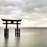 Torii-gate-standing-in-calm-water-under-cloudy-sky