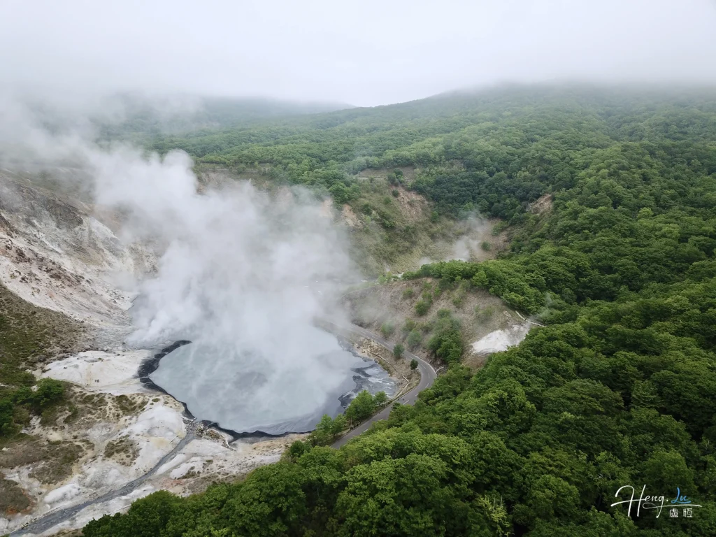 aerial-view-of-steaming-geothermal-valley-surrounded-by-forest-scaled.