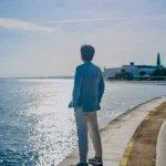 Luheng standing by seaside gazing at sunlit water luheng-standing-by-seaside-gazing-at-sunlit-water